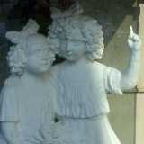 Due bambine con i capelli ricci e un fiocco in testa che si stringono una accanto all�altra: la pi� grande punta il dito in alto, mentre la pi� piccola, che ha un mazzo di fiori in mano, guarda verso il cielo